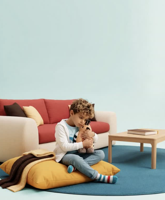 A boy sitting on a yellow cushion hugging Honor